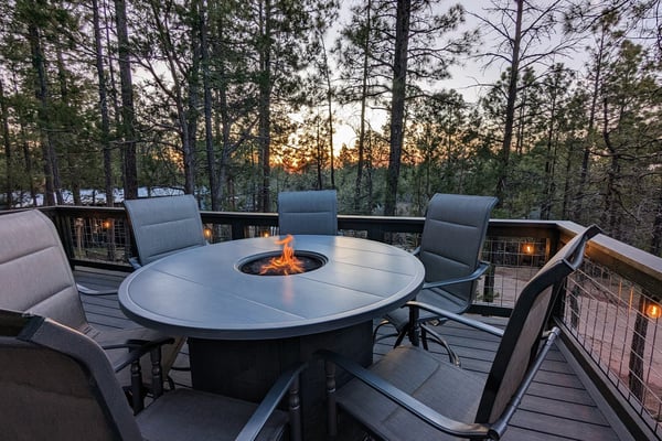 Two modern cabins in forest setting: left shows elevated deck with stairs and railings at dusk; right displays patio with dining furniture and pendant lights.